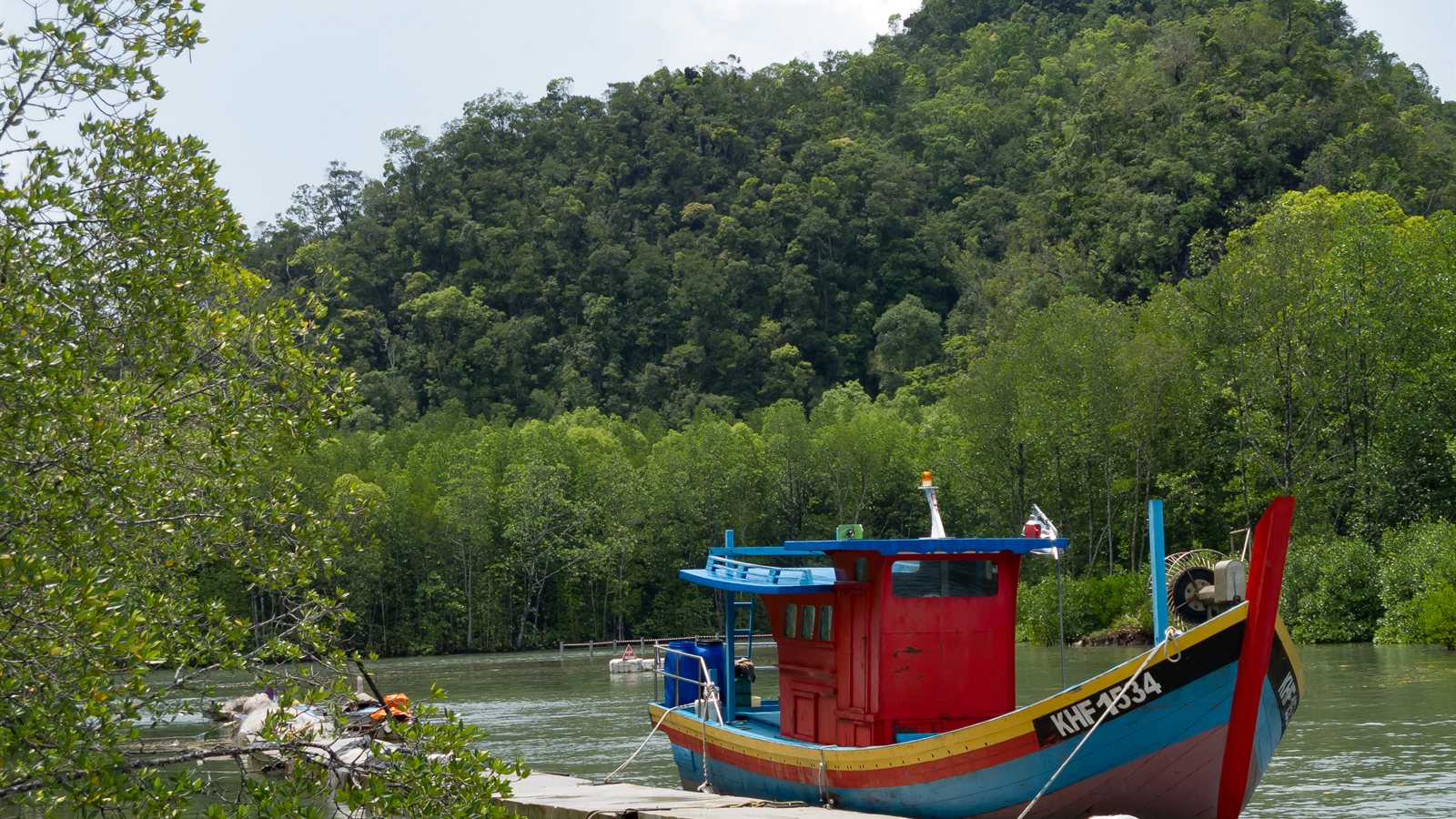 Wooden fishing boat moored at a jetty below forested hills